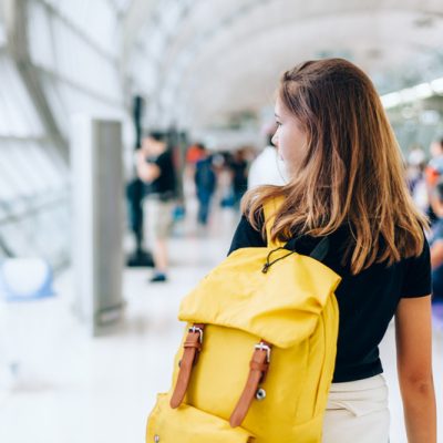 Teen girl waiting for international flight in airport departure terminal. Young passenger with backpack travelling on airplane. Teenager tourizm abroad alone concept.